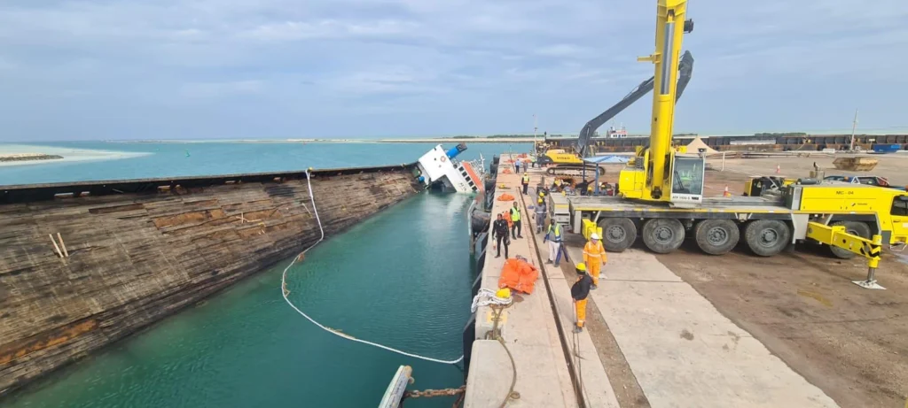 Marine salvage operation showing vessel recovery activities alongside a quay using cranes, lifting equipment, and safety controls.