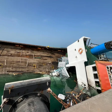 Marine salvage operation showing a partially sunken vessel alongside a quay during recovery operations using cranes and lifting equipment.
