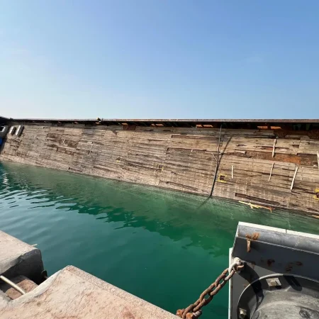 Marine salvage operation showing a partially sunken vessel alongside a quay during recovery operations using cranes and lifting equipment.