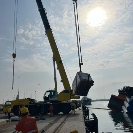 Marine salvage operation showing a partially sunken vessel alongside a quay during recovery operations using cranes and lifting equipment.