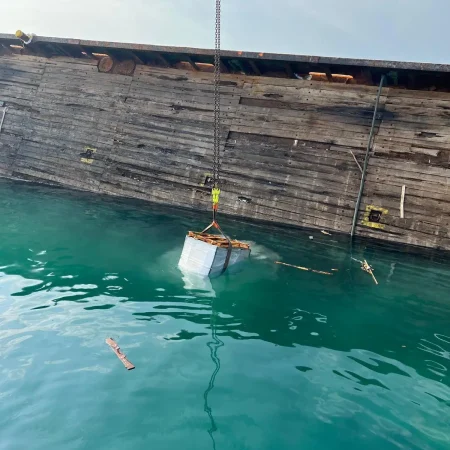 Marine salvage operation showing a partially sunken vessel alongside a quay during recovery operations using cranes and lifting equipment.