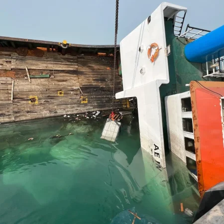 Marine salvage operation showing a partially sunken vessel alongside a quay during recovery operations using cranes and lifting equipment.