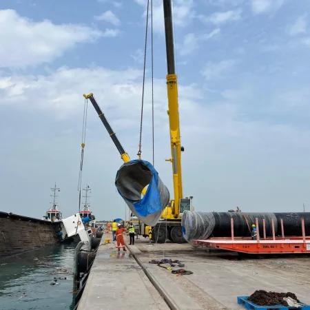 Marine salvage operation showing a partially sunken vessel alongside a quay during recovery operations using cranes and lifting equipment.