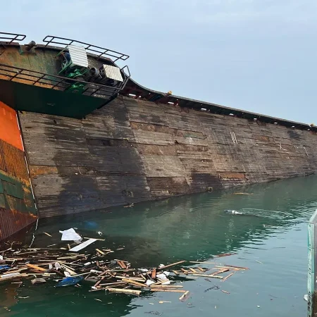 Marine salvage operation showing a partially sunken vessel alongside a quay during recovery operations using cranes and lifting equipment.