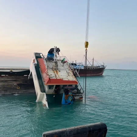 Marine salvage operation showing a partially sunken vessel alongside a quay during recovery operations using cranes and lifting equipment.