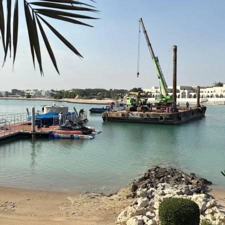 Floating barge equipped with marine piling equipment during installation and positioning of steel marine pipelines inside a port area.