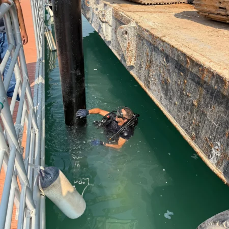 Commercial diver assisting in underwater alignment and stabilization of vertical marine pipeline next to floating platform.