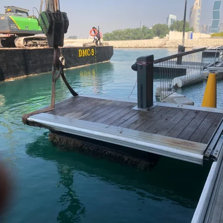 Marine pipeline positioned and stabilized near floating dock with lifting equipment and support structures in a port environment.