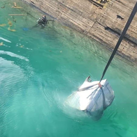Marine salvage operation showing vessel recovery activities alongside a quay using cranes, lifting equipment, and safety controls.