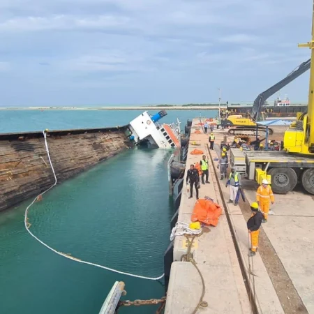 Marine salvage operation showing vessel recovery activities alongside a quay using cranes, lifting equipment, and safety controls.