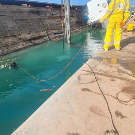 Marine salvage operation showing vessel recovery activities alongside a quay using cranes, lifting equipment, and safety controls.