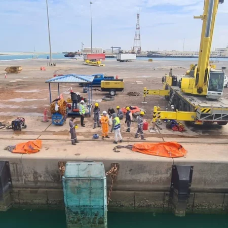 Marine salvage operation showing vessel recovery activities alongside a quay using cranes, lifting equipment, and safety controls.