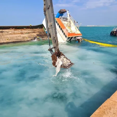 Marine salvage operation showing vessel recovery activities alongside a quay using cranes, lifting equipment, and safety controls.